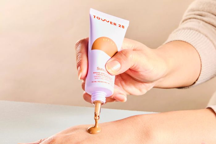 An individual applies Tower 28 SunnyDays SPF 30 Tinted Sunscreen onto their hand