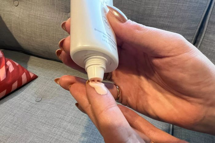 Two hands placing a drop of Supergoop! Glowscreen on their fingertip