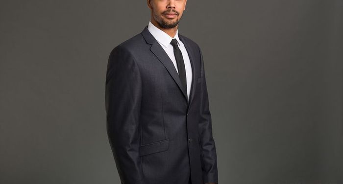 A professional young businessman dressed sharply in a studio against a neutral grey backdrop.