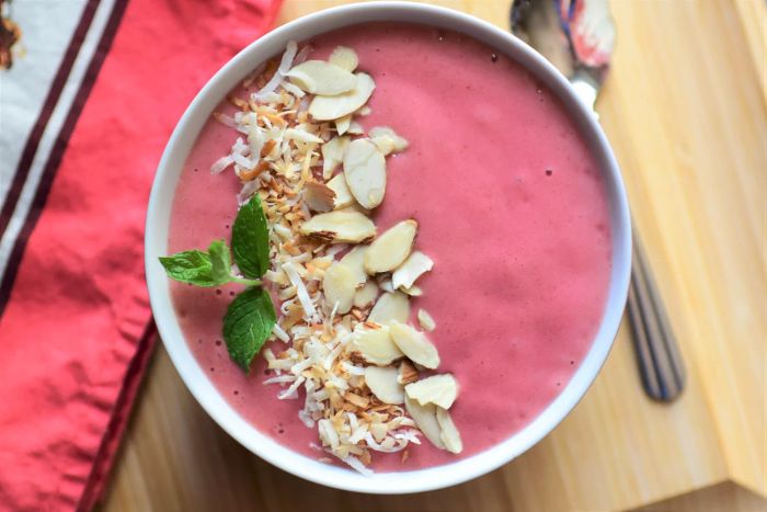 A strawberry smoothie bowl garnished with slivered almonds, coconut flakes, and a sprig of mint.