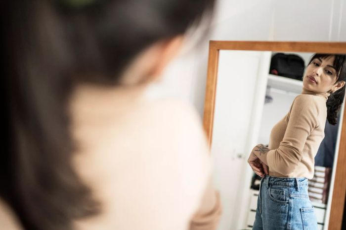 A woman checking herself out in a pair of jeans in front of a mirror