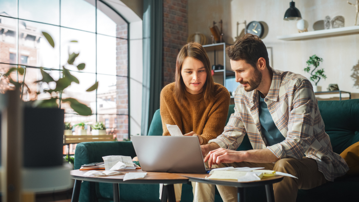A Couple Managing Stressful Financial Tasks at Home: Young Family Filling Out Tax Forms, Sorting Mortgage Documents, Bills, Checks, and Invoices While Sitting on the Sofa in Their Apartment