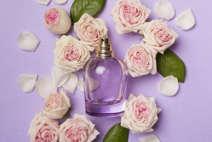 A bottle of perfume surrounded by rose petals, shot from above against a vibrant backdrop.