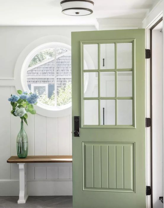 Green paint on the front door of the home entryway, with a vase of flowers placed on the sideboard.