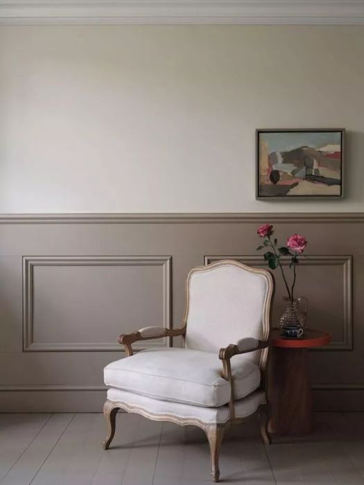 London Stone-like greige paint on the walls, with darker wainscoting below and a beige armchair.