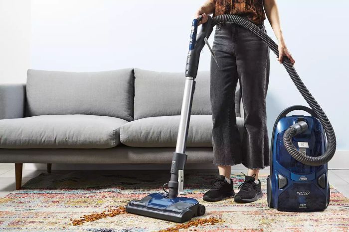 A person is using a Kenmore Pet Friendly Pop-N-Go Vacuum to clean a rug in front of a sofa.