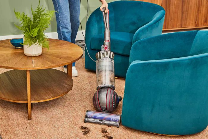 A person is using the Dyson Ball Animal 3 Extra to clean around furniture on a rug.