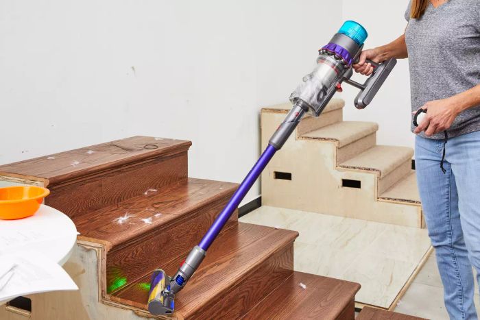 A person is shown using the Dyson Gen5detect Cordless HEPA Vacuum to clean a wooden staircase.