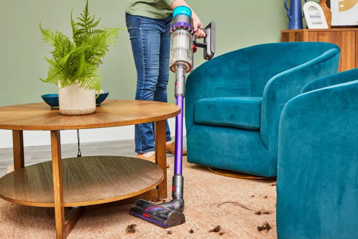 A person is seen using the Dyson Gen5detect Cordless HEPA Vacuum to clean in the area around furniture.