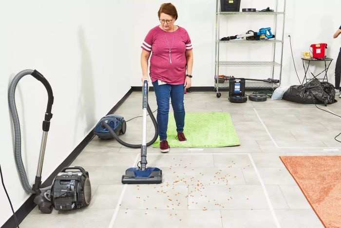 A person is vacuuming pet food from a tile floor with the Kenmore Pet-Friendly POP-N-GO Bagged Canister Vacuum.