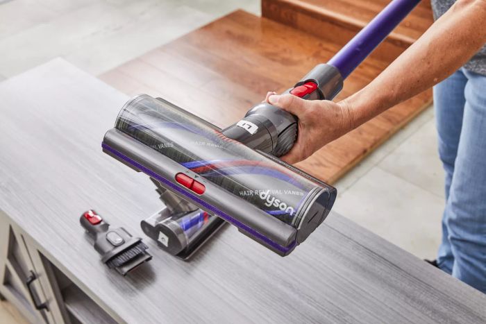 A hand grips the Dyson Gen5detect Cordless HEPA Vacuum, with the attachments visible in the background.