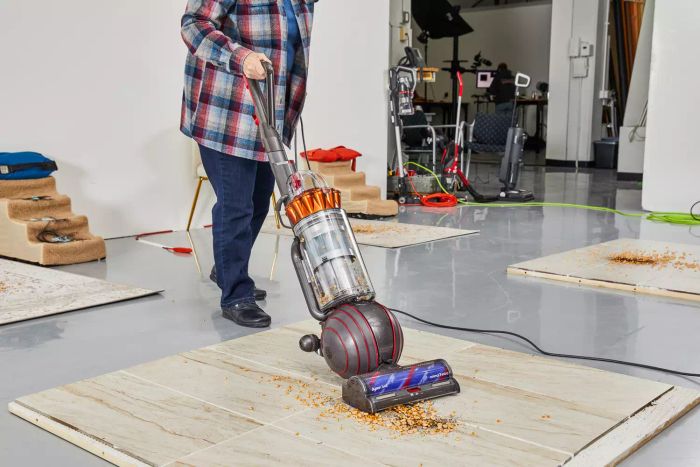A person is cleaning food debris from a tile floor with the Dyson Ball Animal 3 Extra.