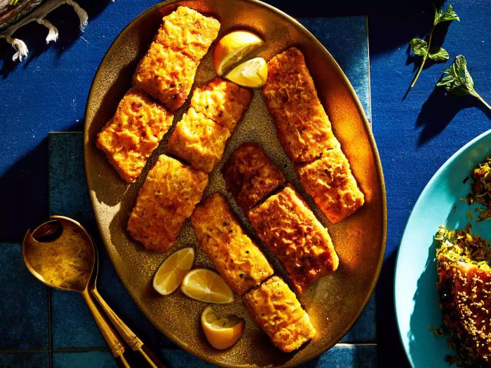 pieces of fried fish on platter with lemon wedges on blue background