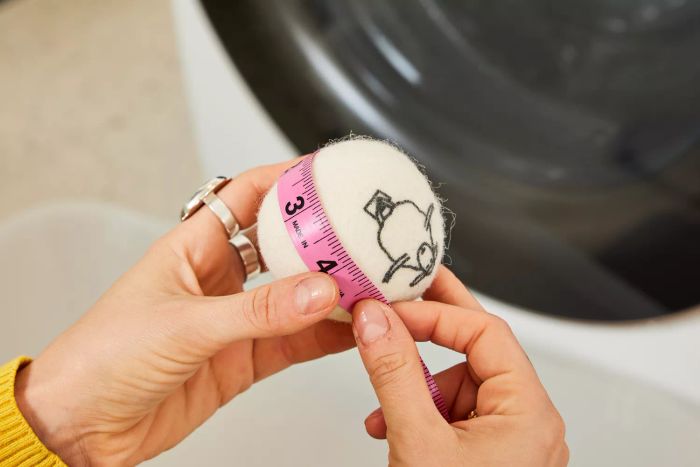An individual is seen taking measurements of the Kainga Recka Wool Dryer Ball.