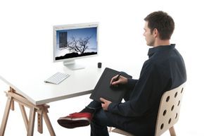 An artist sketching on a Wacom tablet connected to a computer.