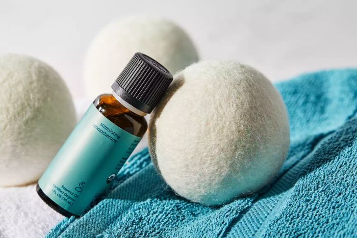 A bottle of Eucalyptus essential oil positioned next to the Grove Co. Wool Dryer Balls.