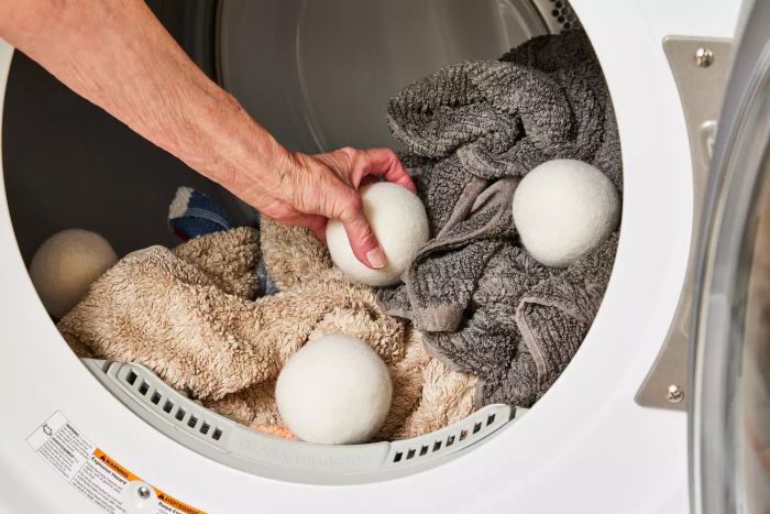 An individual placing the Everspring 100% New Zealand Wool Dryer Balls into a dryer loaded with laundry