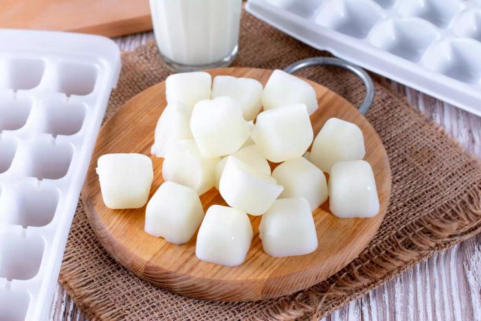 Frozen milk cubes placed on a cutting board over a white wooden surface