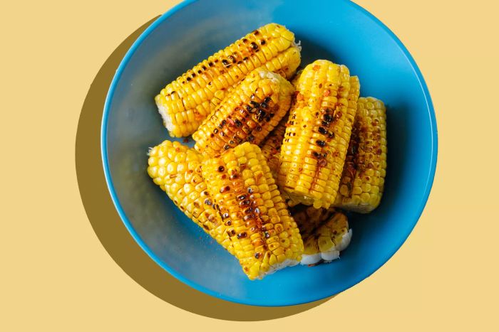 Grilled yellow corn cobs, topped with spices and served on a vibrant ceramic plate, set against a rustic wooden table. This showcases the essence of homemade cooking. Perfect for vegetarian, vegan, and lean meals.