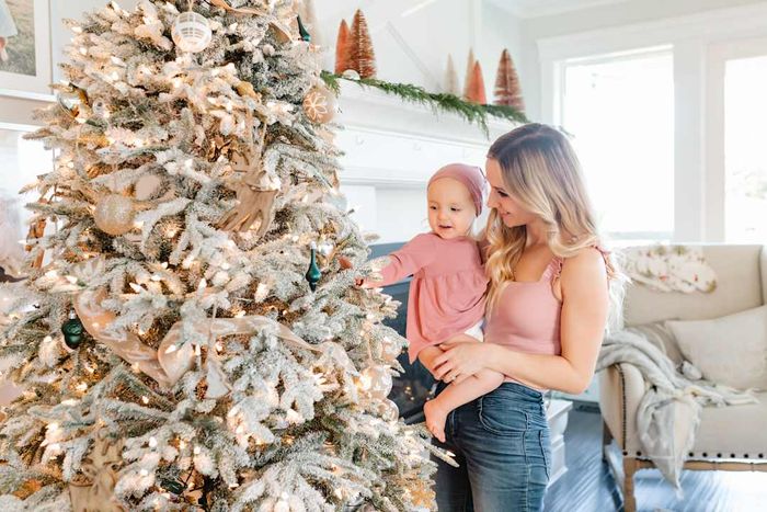 A mother embraces her baby daughter beside a beautifully adorned Christmas tree.