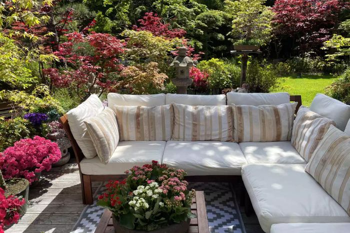 A decorative Japanese-inspired garden complete with an outdoor seating area. The space includes whitewashed, grooved timber decking, Japanese bonsai maples, hardwood elements, and cushioned seating surrounding an outdoor plastic rug.