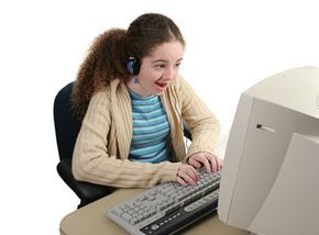 A teenage girl happily chats with her friends using instant messaging on her desktop computer.