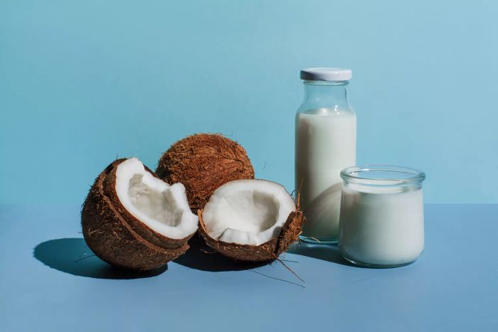 A visual of coconuts alongside milk and cream against a blue backdrop.