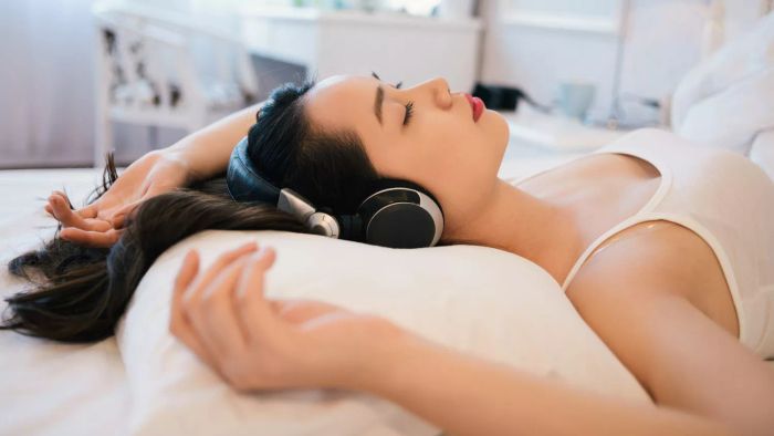 A Woman Lying in Bed, Her Head Resting on a Pillow, Eyes Closed, Wearing Over-Ear Headphones