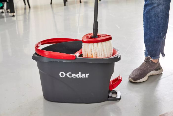 A person holds the mop from the O-Cedar EasyWring Spin Mop and Bucket System displayed on a tile floor