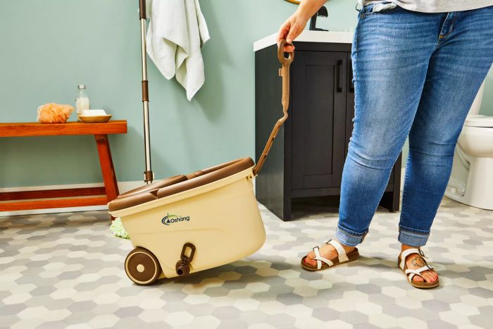 A person pushes the Oshang Spin Mop and Bucket across a bathroom's tiled floor.