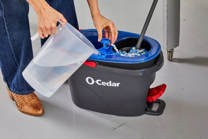 A person pours water into the reservoir of the O-Cedar EasyWring RinseClean Spin Mop & Bucket System