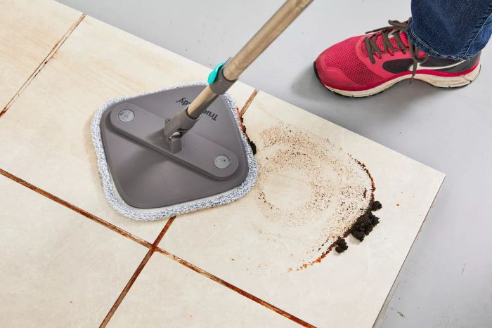Person cleaning dirty tile flooring using the True & Tidy TrueClean Spin Mop and Bucket System