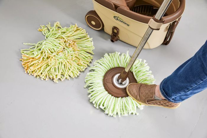 A person steps on the base of the Oshang Spin Mop and Bucket to operate it.