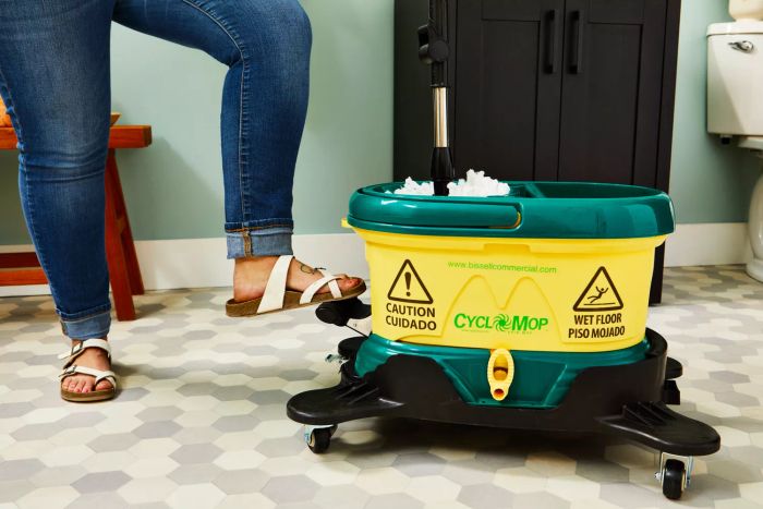 A person steps on the spin pedal of the Bissell Commercial CycloMop Spin Mop in a bathroom.