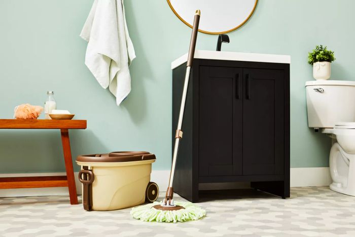 The Oshang Spin Mop and Bucket rests against a sink cabinet beside a bench.