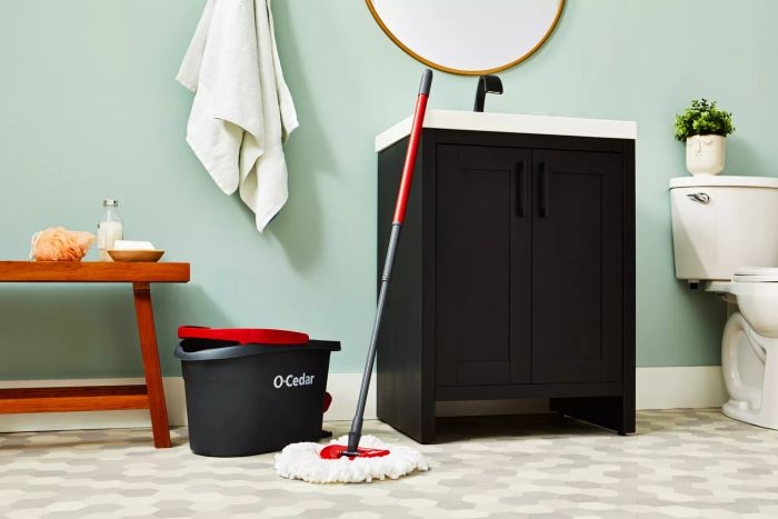 The O-Cedar EasyWring Spin Mop and Bucket System displayed in a bathroom on a tile floor, positioned between a wooden bench and sink