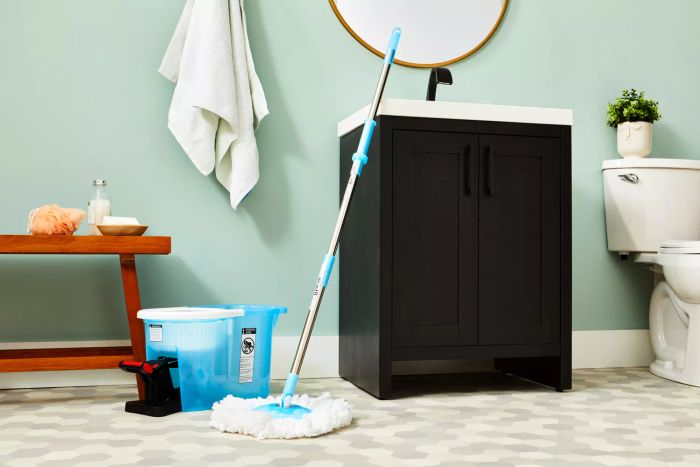 The Hurricane Spin Mop rests against a sink in a bathroom on tile flooring.
