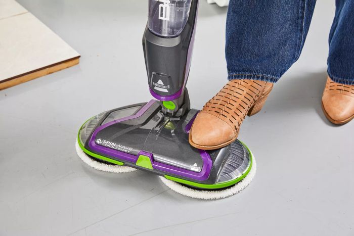 A person steps on the base of the Bissell SpinWave Cordless PET Hard Floor Spin Mop.