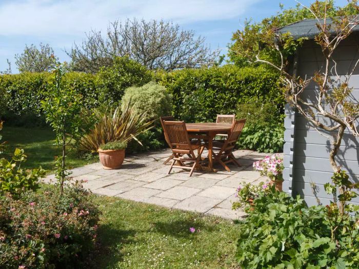 A private patio featuring tall shrubs and plants alongside wooden outdoor furniture