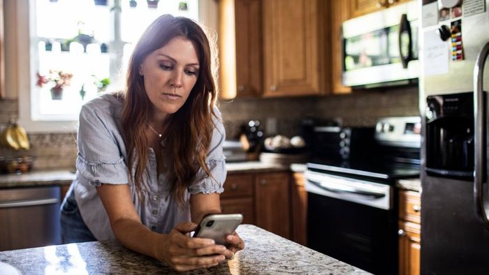A woman is using her mobile phone in the kitchen at home.