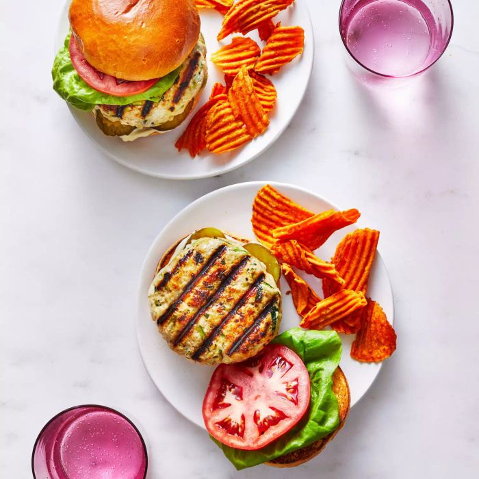 Open-face grilled turkey and zucchini burgers served with a side of chips on a white plate.