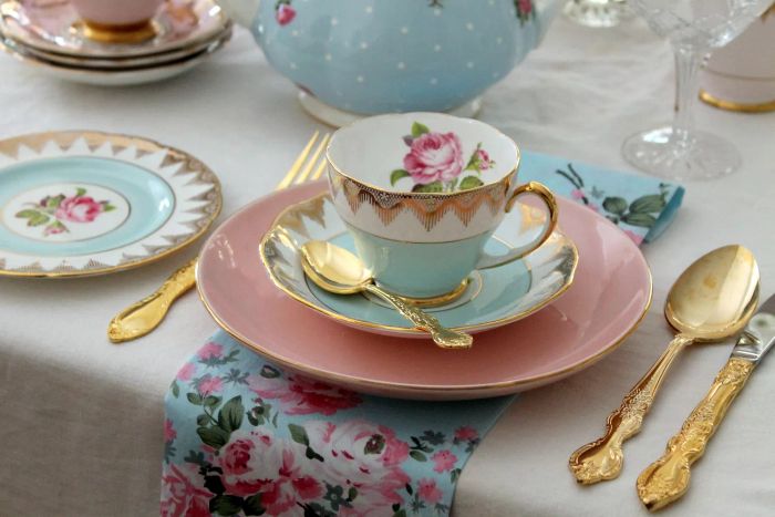 Vintage high tea party setup with pink and blue tea cups, plates, gold flatware, pink roses, and a beautifully arranged place setting – perfect for a wedding or bridal shower.
