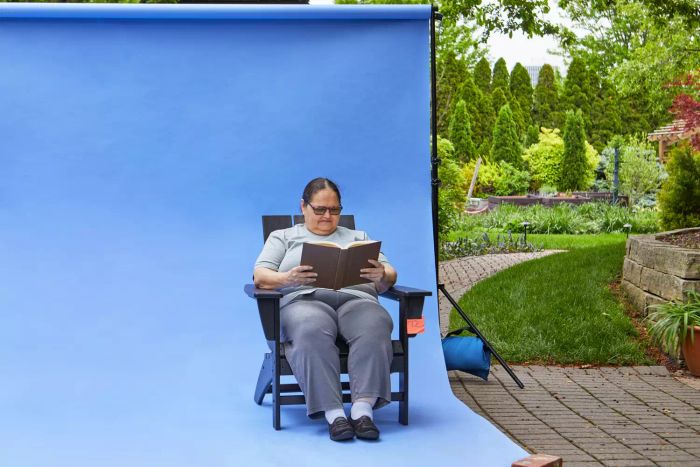 A person sitting on the Polywood Modern Adirondack Chair while reading a book in front of a blue screen