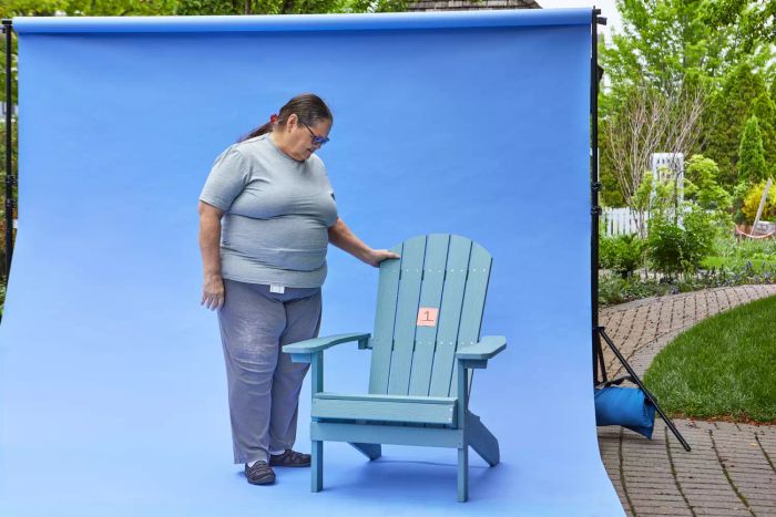 A woman stands beside a YEFU Adirondack Chair with a blue backdrop behind her.