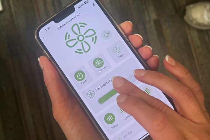 A person adjusts the fan's speed using their smartphone app.
