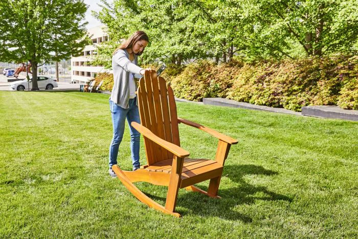 A person pushing the World Market Slatted Wood Adirondack Rocking Chair forward on a lawn.