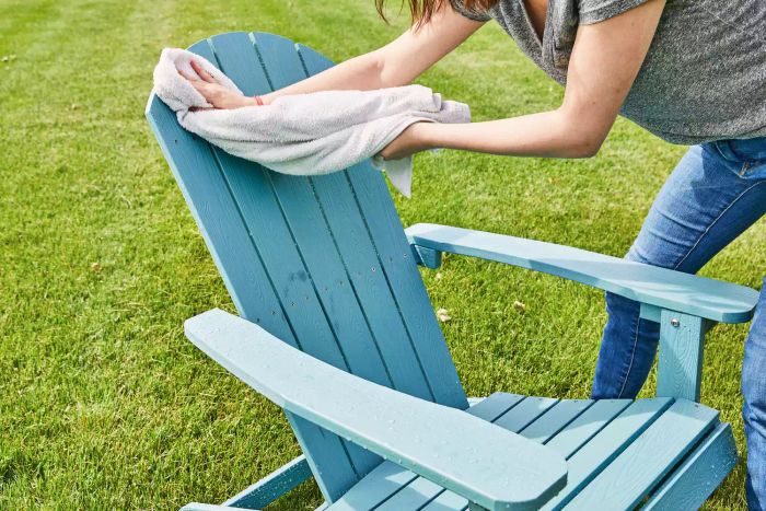 A person is wiping the Yefu Plastic Adirondack Chair outdoors with a white towel.