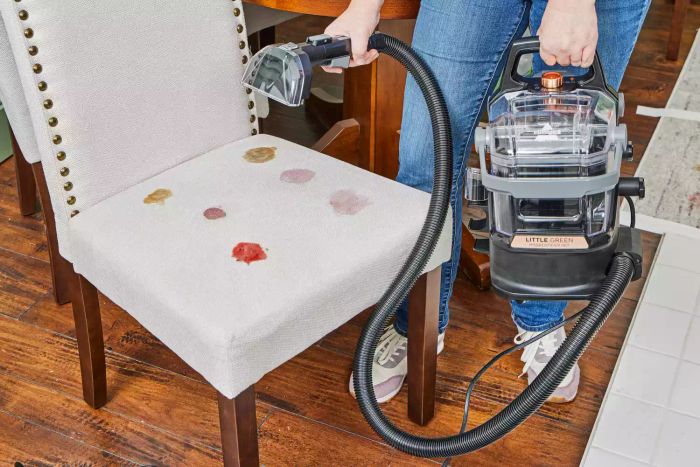 A person hovers the Bissell Little Green HydroSteam Pet Carpet Cleaner over a chair marked with a stain