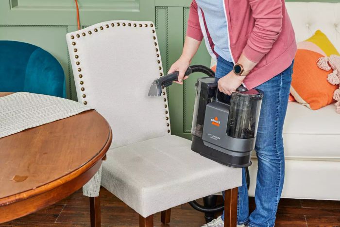 A person cleaning a chair with the Bissell Little Green Cordless Portable Carpet Cleaner.