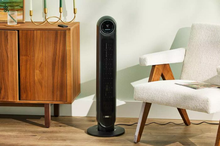 Dreo Nomad One Tower Fan positioned between a chair and a sideboard